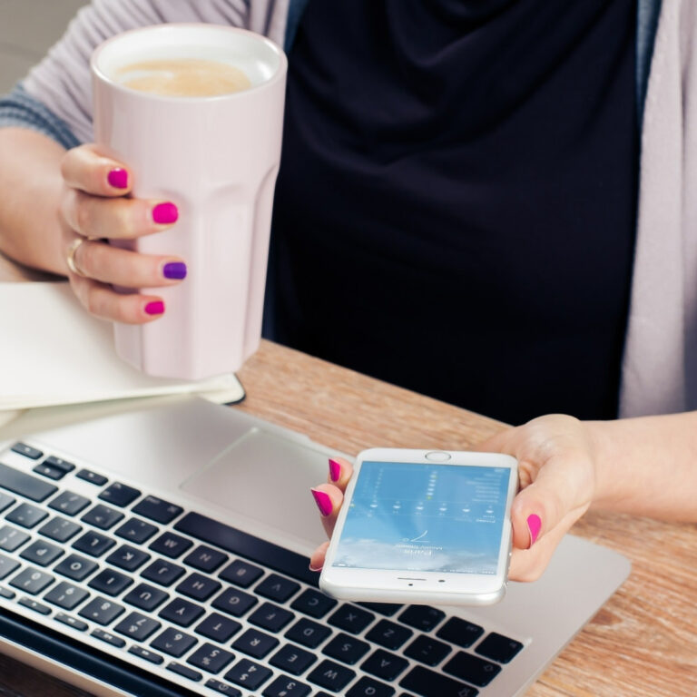 lady working at desk with a cup of coffee in hand and smartphone
