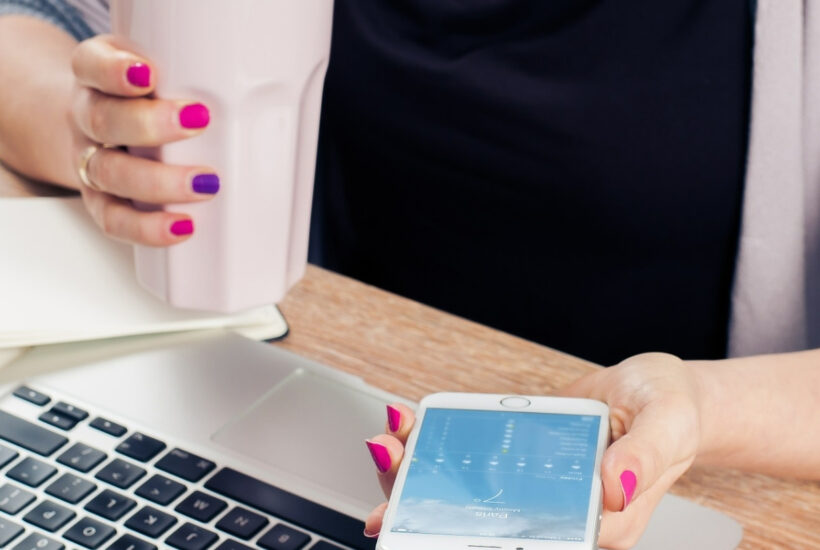 lady working at desk with a cup of coffee in hand and smartphone