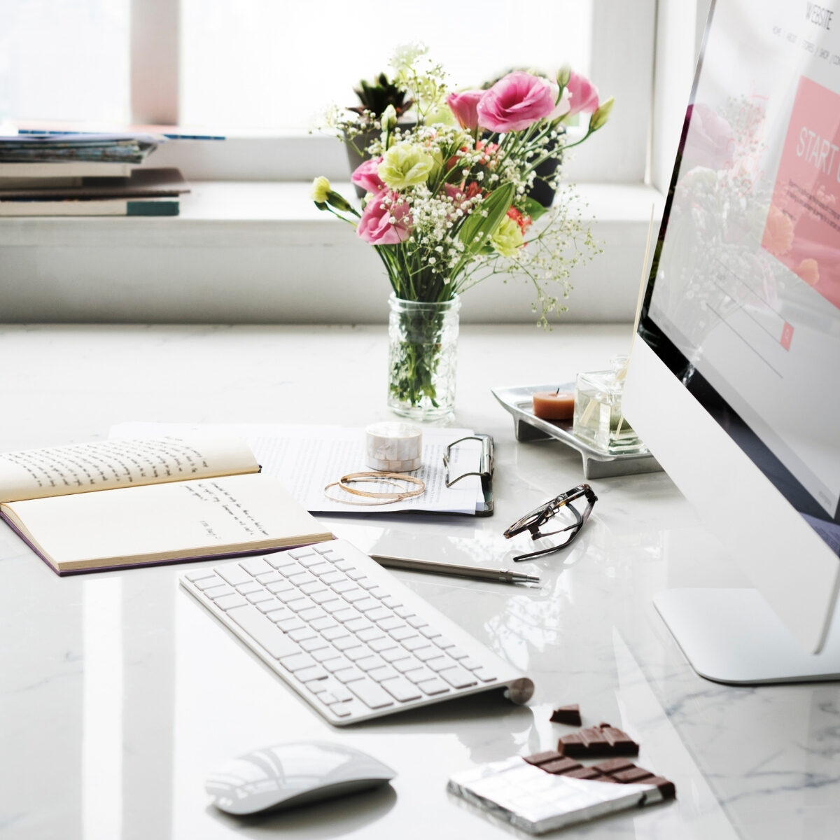 desk view of Mac monitor, keyboard, mouse, and a vase of mixed flower bouquet