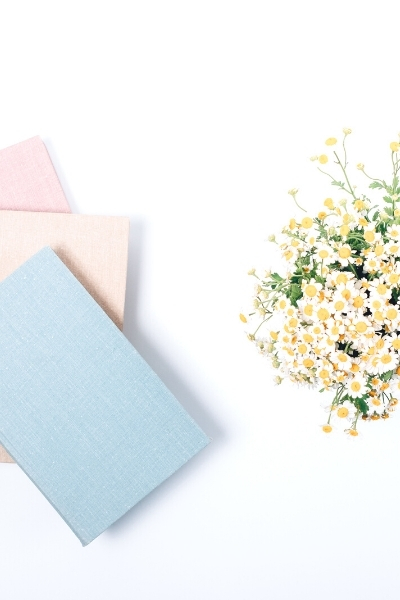 three journals stacked in pastel shades of blue, peach, and pink with small white flower bouquet on a table top 
