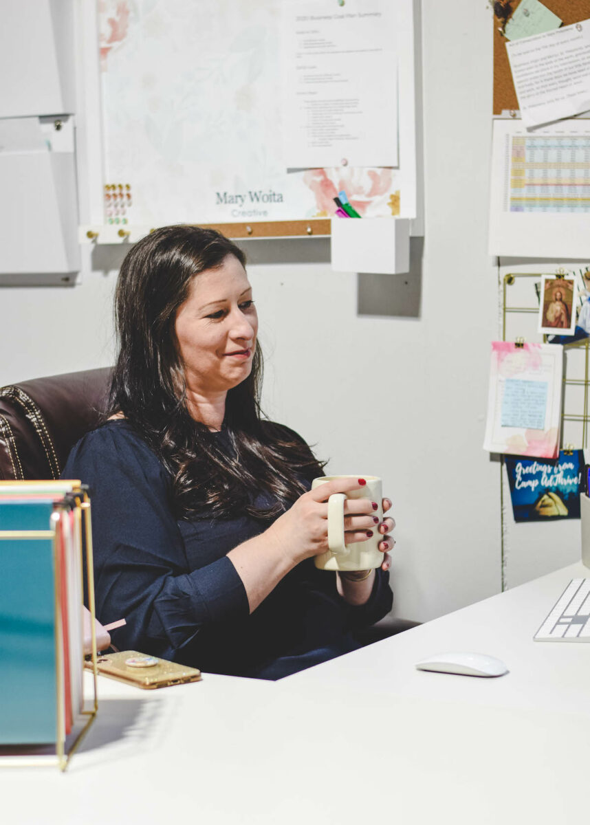 sitting at the desk and holding a white mug of coffee