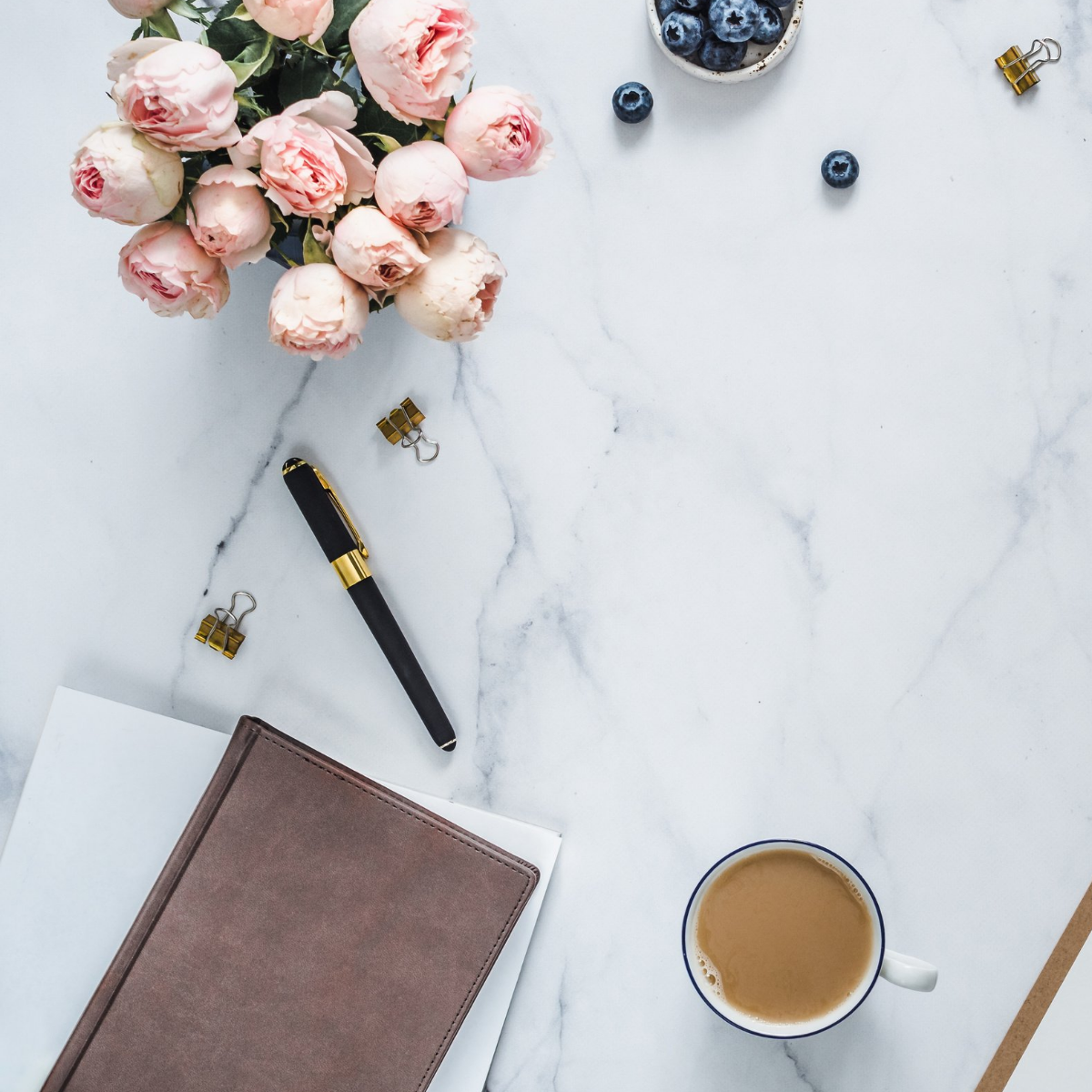 cup of coffee next to a lined notebook and pen…and light pink roses in a vase