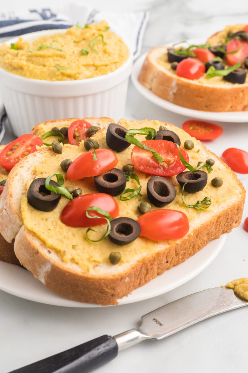 bread with hummus and tomatoes and black olives over top.